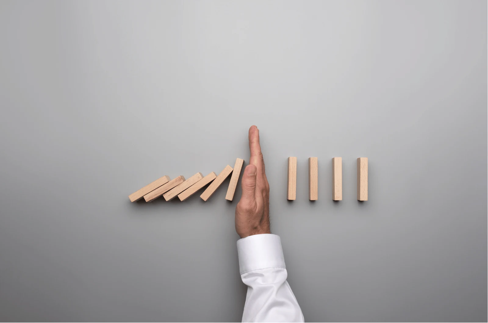 A hand stopping a row of falling wooden blocks before it reaches the ones still standing