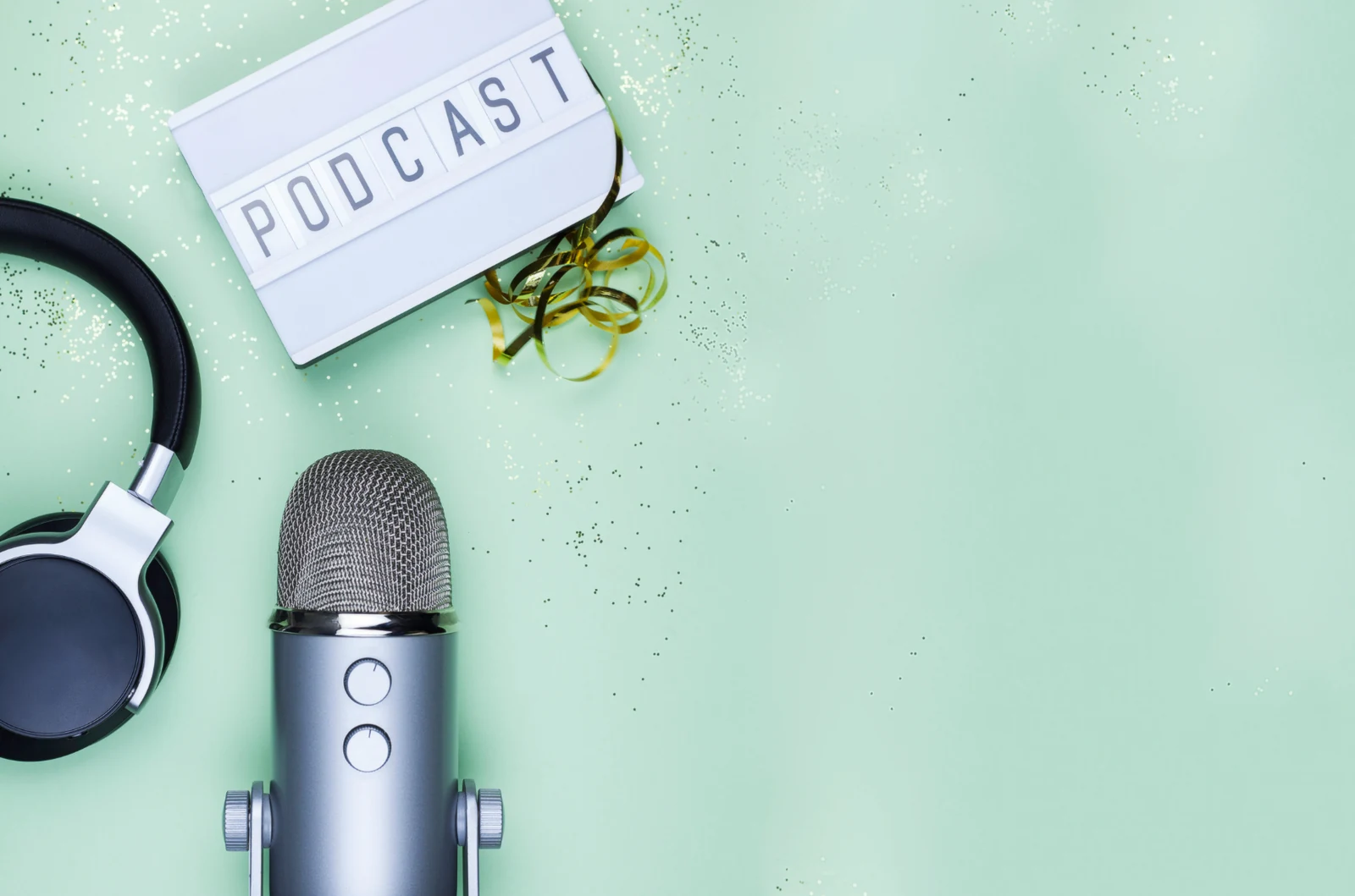A microphone, a pair of headphones and a sign reading PODCAST on a mint green background